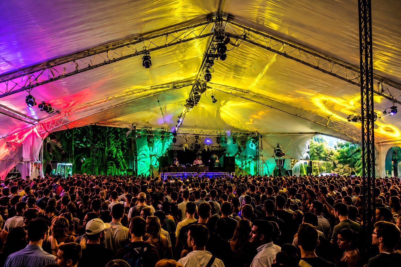 Panoramic festival crowd facing a stage beneath a colorful tent