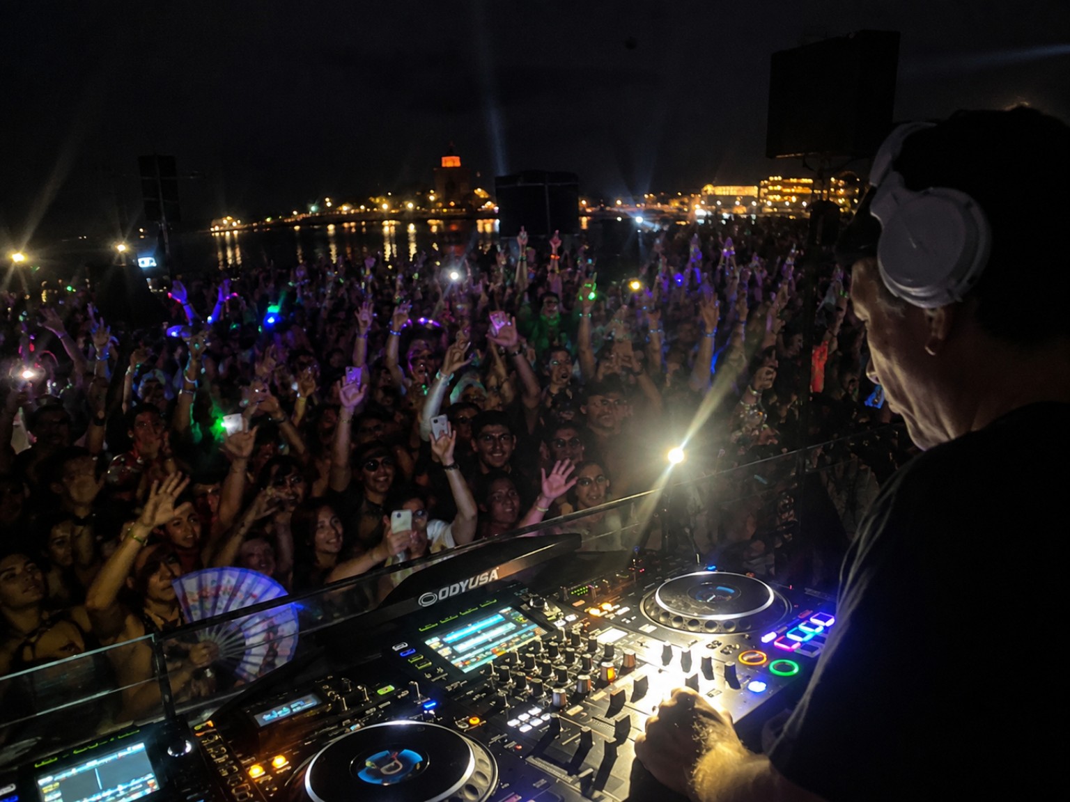 DJ performing for a large nighttime waterfront crowd